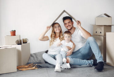 Will Insurance Pay for Hail Damage to a Metal Roof? - A Picture of a Couple Holding a Baby and a Roof-Angled Cardboard Slat Over their Head