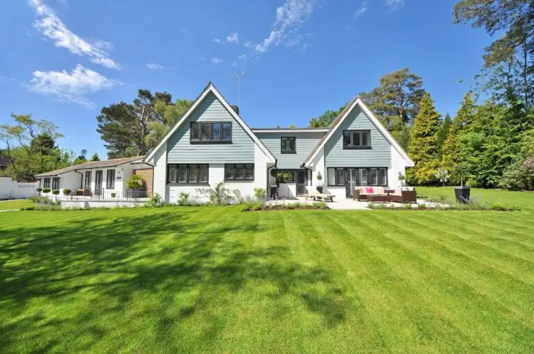 White and gray house with a big yard and lots of greenery.