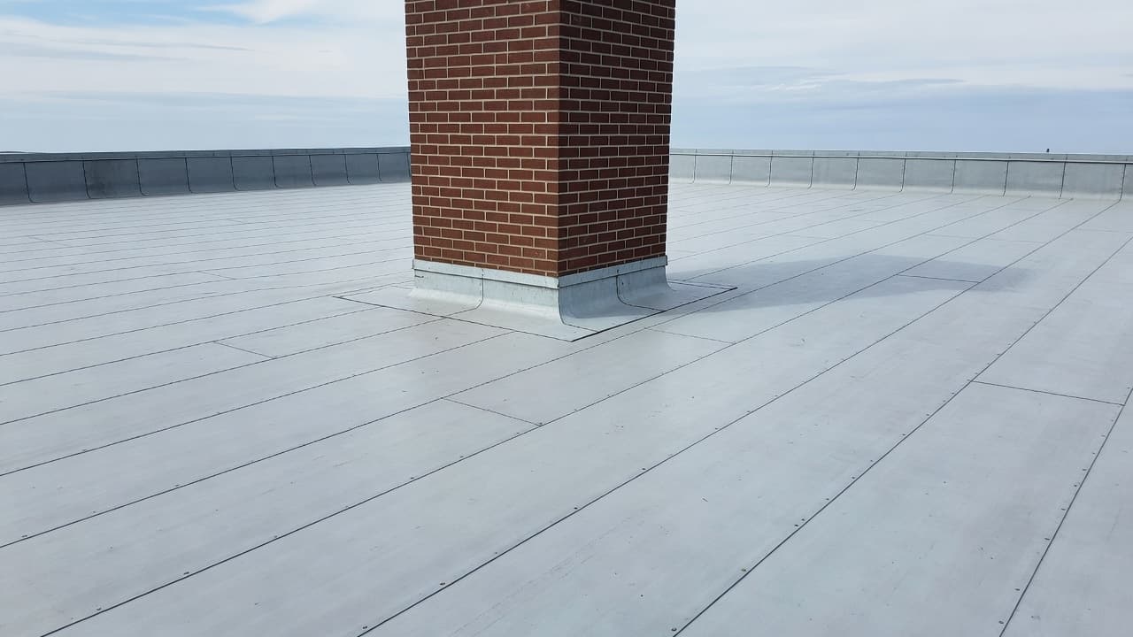 Can a Chimney Cricket Leak Without Missing Shingles? A clean, well-maintained flat roof features a central masonry chimney stack standing against a clear sky. The industrial rooftop surface shows consistent gravel texture around the prominent brick ventilation structure.