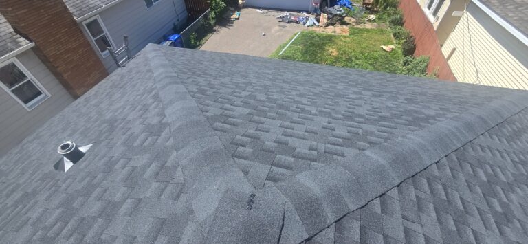 Residential roof layout Gray asphalt-shingle roof with intersecting capped hips and a vent pipe beside neighboring homes.