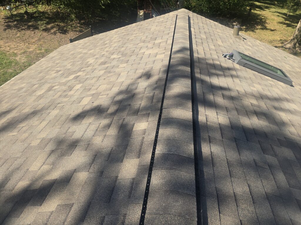 Roofing Contractor in Saint Anthony Village, MN Tan asphalt-shingle roof with a ridge vent, skylight, vent pipe, and tree shadows.